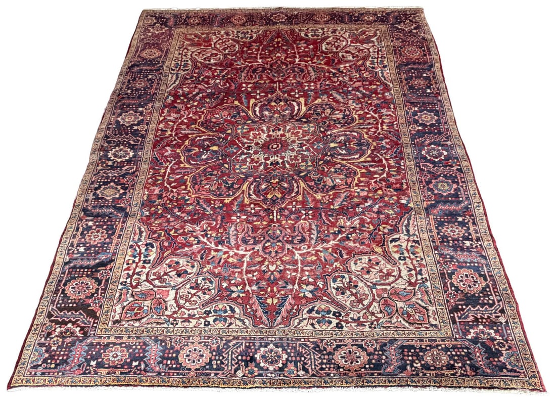 MID 20TH - CENTURY NORTHWEST PERSIAN HERIZ CARPET: CIRCA 1940, enclosed by spandrels of complementary design. The composition framed by a deep indigo border with stylised rosettes and vinery, flanked by multiple guard stripes. CARPETS AND RUGS