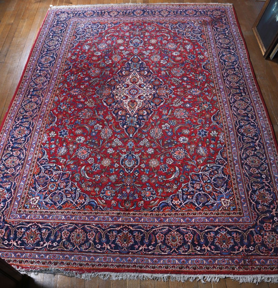 LARGE PERSIAN RED GROUND CARPET: The field with an all-over arrangement of stylised floral motifs and medallions within multiple borders, in a palette of deep red, blue, and ivory. CARPETS AND RUGS