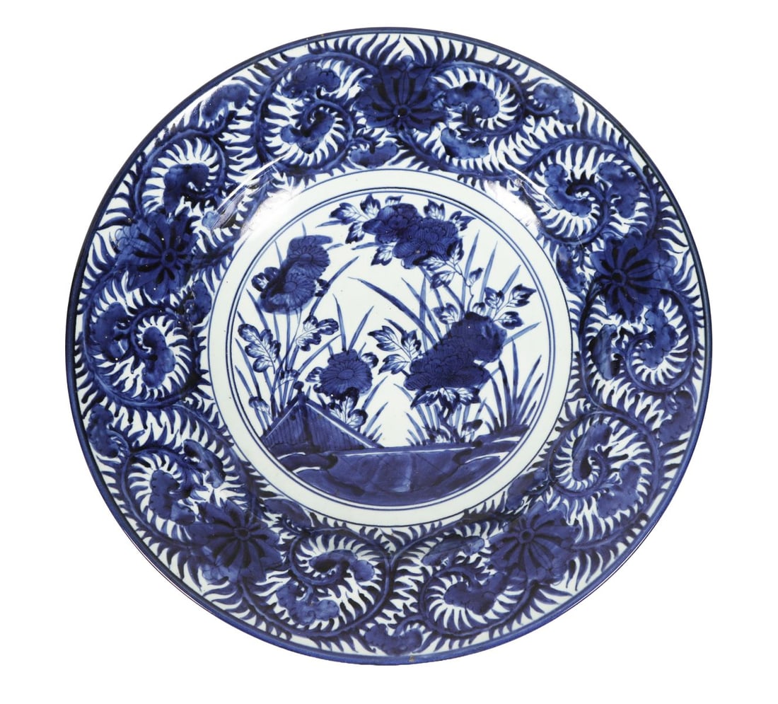 19TH CENTURY JAPANESE BLUE AND WHITE CHARGER: A very large 19th-century Japanese charger, painted in underglaze blue with bold foliate scroll borders surrounding a central floral reserve. JAPANESE