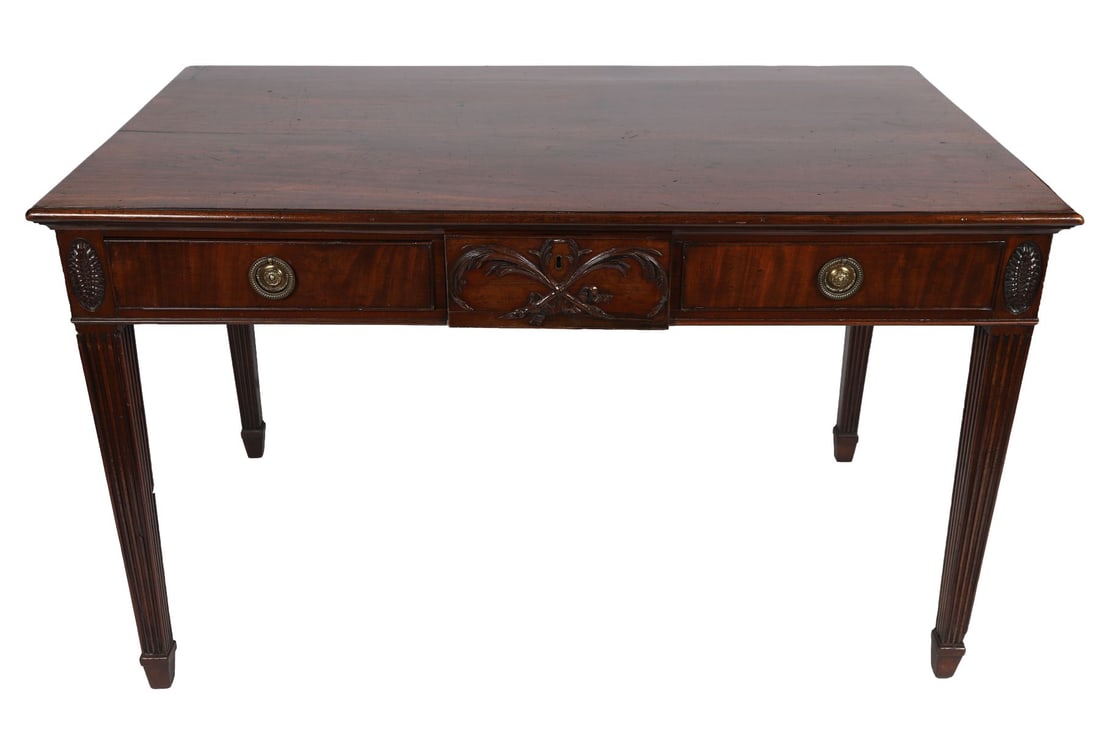 GEORGE III MAHOGANY SERVING TABLE: IN THE MANNER OF ROBERT ADAM, The rectangular top above a frieze centred with a carved tablet and flanked by drawers, raised on fluted tapering legs terminating in block feet. FURNITURE