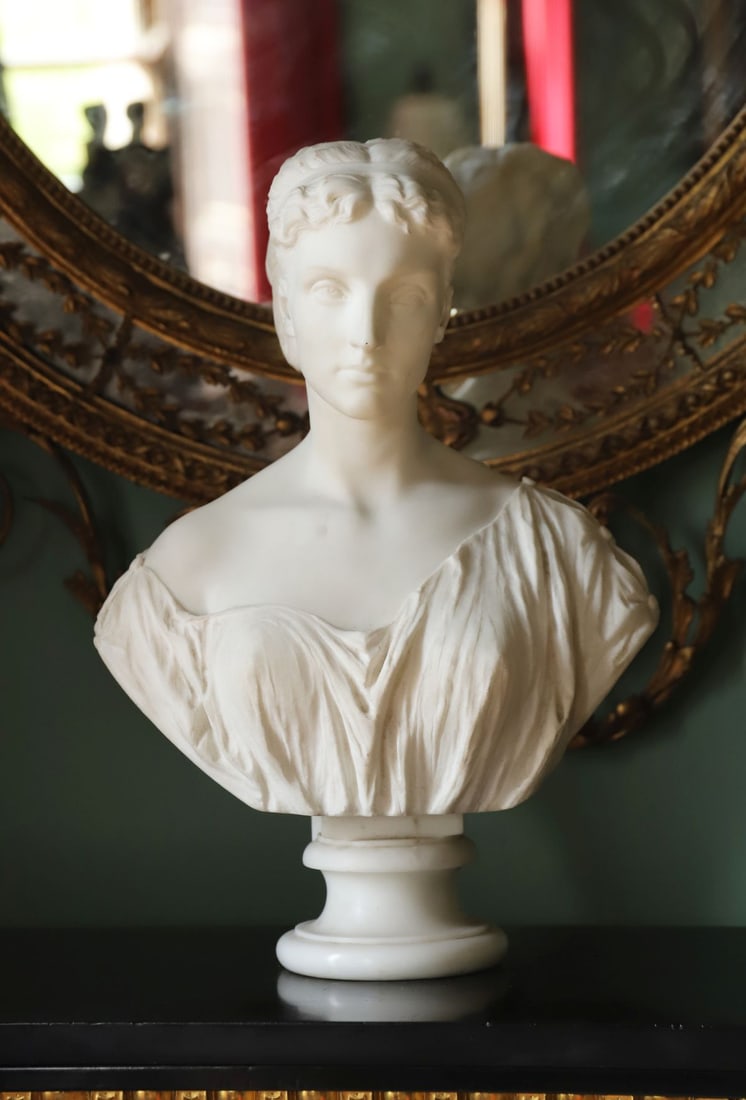 19TH-CENTURY CARVED WHITE MARBLE BUST: A 19th-century carved white marble bust of a young woman, her hair bound with a headband, shown in classical dress with finely carved drapery, raised on a circular socle. SCULPTURE