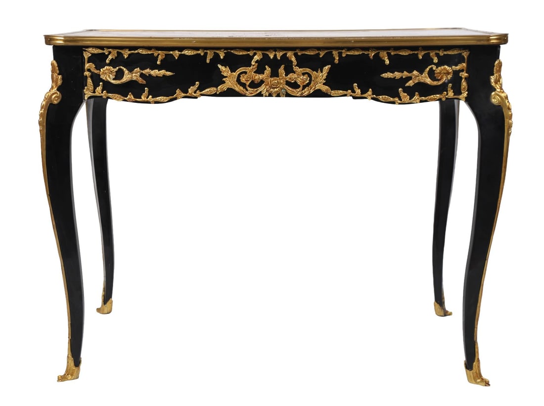 FRENCH EBONISED &GILT-METAL MOUNTED WRITING TABLE: LATE 19TH CENTURY, A French ebonised writing table of serpentine outline, the top inset with a decorative panel and enclosed by a moulded gilt-metal border, above a frieze drawer, raised on slender ca
