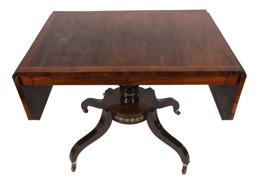 REGENCY ROSEWOOD & ORMOLU-MOUNTED SOFA TABLE: SATINWOOD CROSSBANDED, The rectangular top with drop leaves and crossbanded border above a frieze fitted with drawers, raised on a turned column and platform base with downswept legs and castors. FURN