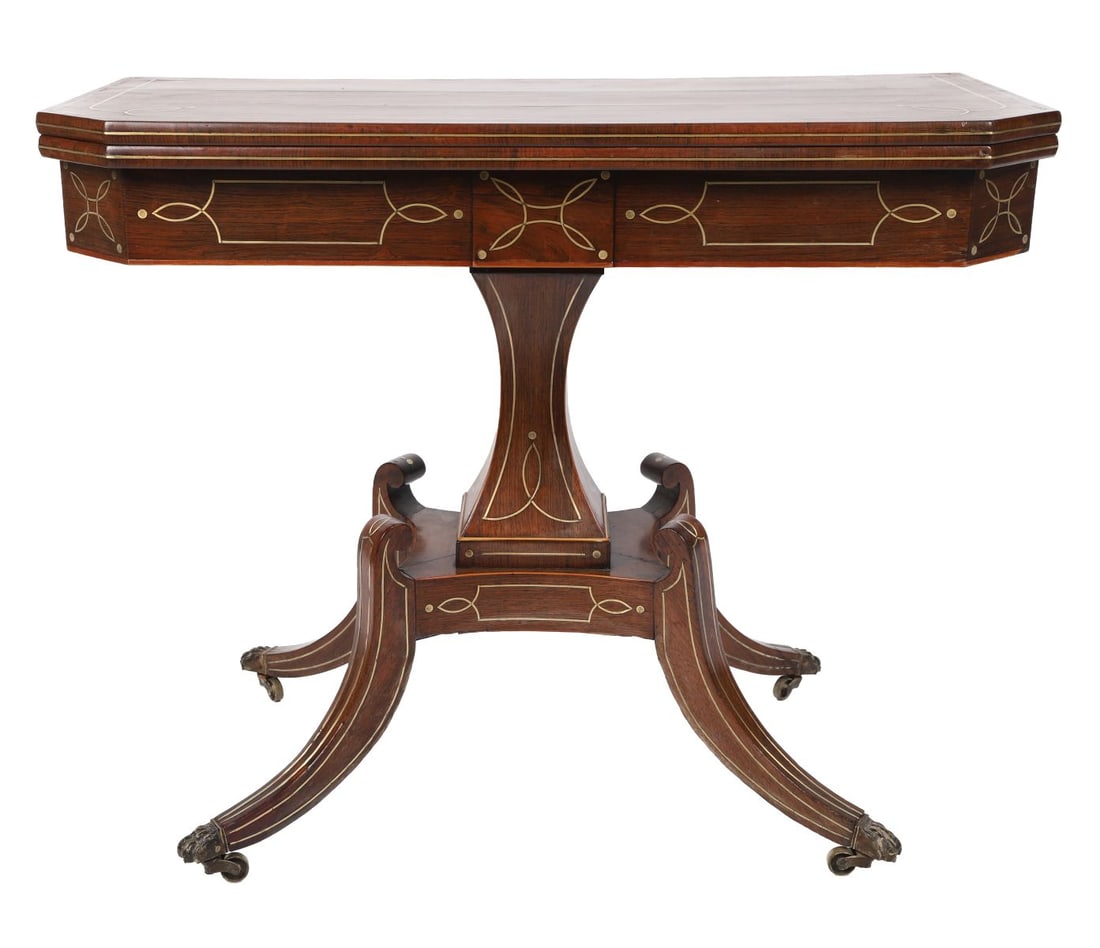 REGENCY ROSEWOOD AND FOLD-OVER CARD TABLE: BRASS-INLAID, The rectangular top with brass line inlay opening to a baize-lined interior above a frieze with further brass inlay, raised on a central support with splayed legs terminating in brass ca