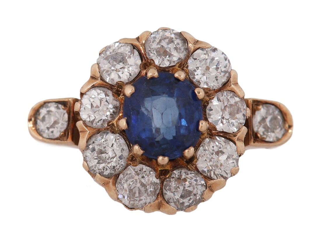 SAPPHIRE AND DIAMOND CLUSTER RING: Ring set with a central blue stone within a surround of brilliant-cut diamonds, in white metal mount. JEWELLERY