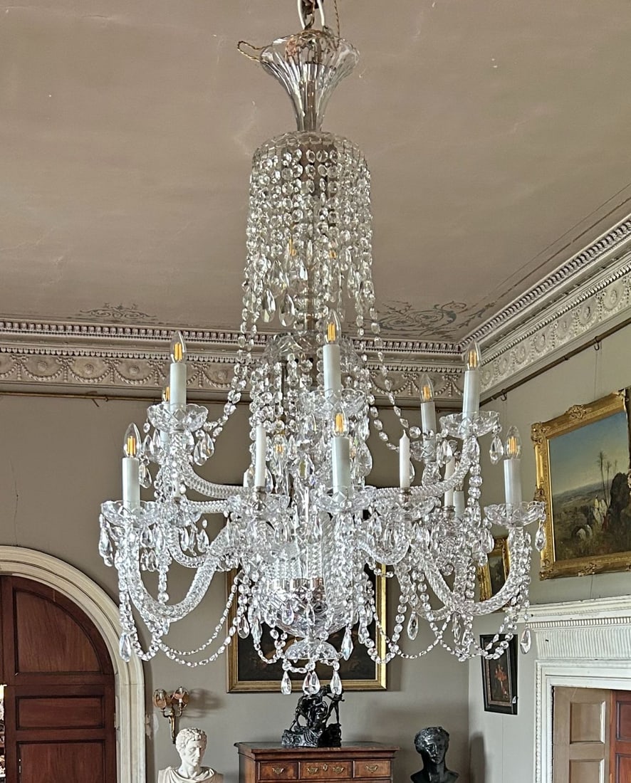 LARGE IRISH CUT CRYSTAL EIGHTEEN-LIGHT CHANDELIER: With tiered baluster stem issuing scrolling arms, hung with faceted drops and swags, suspended from a chain. LIGHTING