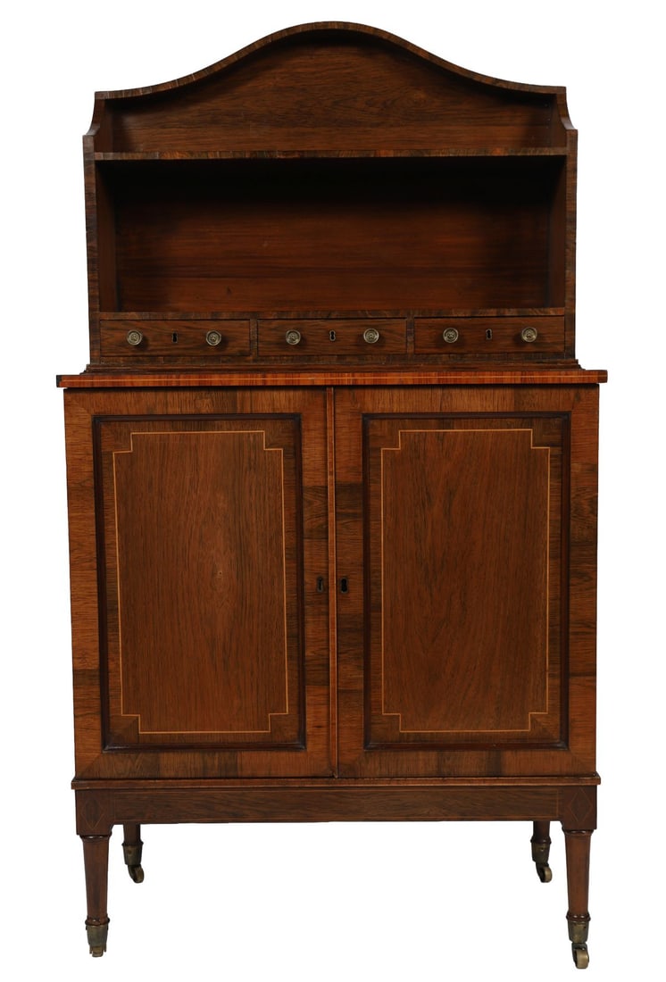 REGENCY ROSEWOOD OPEN BOOKCASE: Of shaped outline with a scrolled pediment above a single open shelf and a series of small drawers, the base with two panelled cupboard doors, raised on slender tapering legs terminating in castors. F