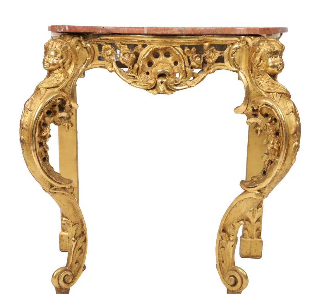 18TH - CENTURY CARVED GILTWOOD CONSOLE TABLE: An 18th-century carved giltwood console table, the serpentine marble top above a richly pierced apron with scrolling foliate ornament and masks, raised on cabriole legs carved with putti and acanthus.