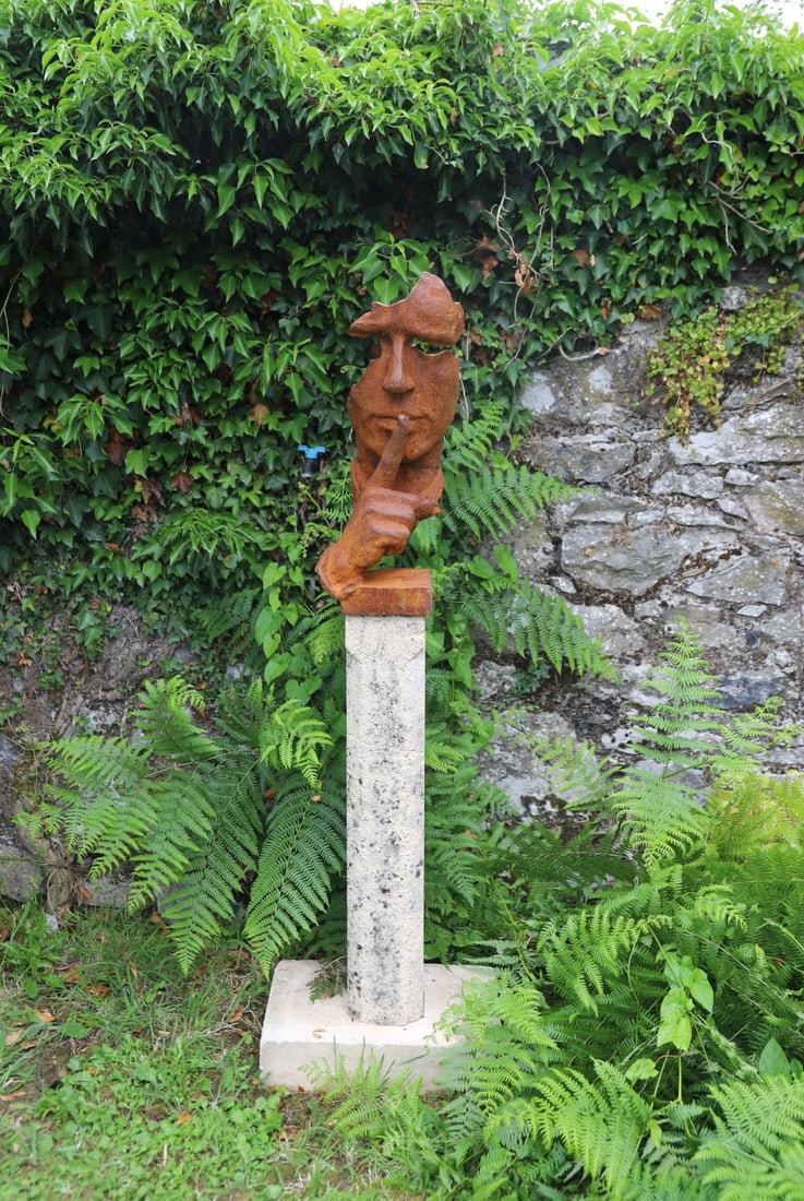 CAST IRON GARDEN SCULPTURE: depicting Silence, after Salvador Dali, mounted on a carved moulded sandstone base.