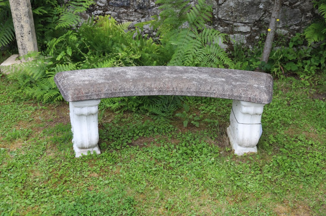 COMPOSITE STONE CURVED GARDEN BENCH: A curved composite stone garden bench with shaped top and scroll-ended supports. Weathered finish with lichen and patina throughout.