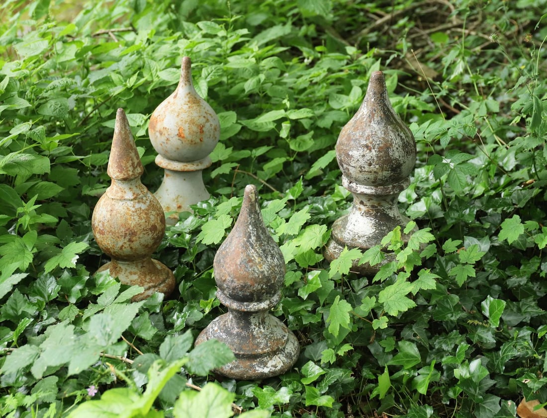 LOT OF FOUR CAST IRON FINIALS: Lot comprising four cast iron finials of baluster and flame-form design, retaining traces of original paint and weathered surface.