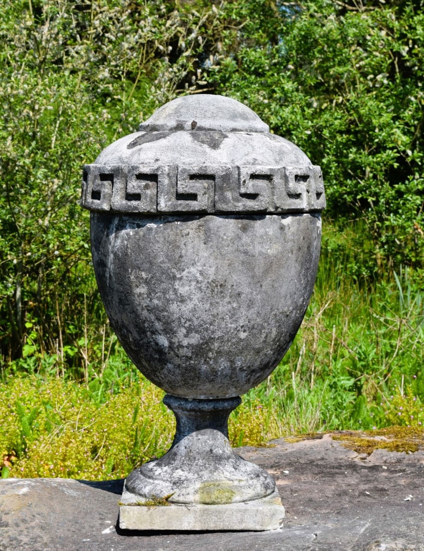 18TH-CENTURY SANDSTONE STONE LIDDED GARDEN URN: Composite stone garden urn and cover of classical ovoid form, decorated with a Greek key band and raised on a circular socle and square base. Weathered patination throughout.