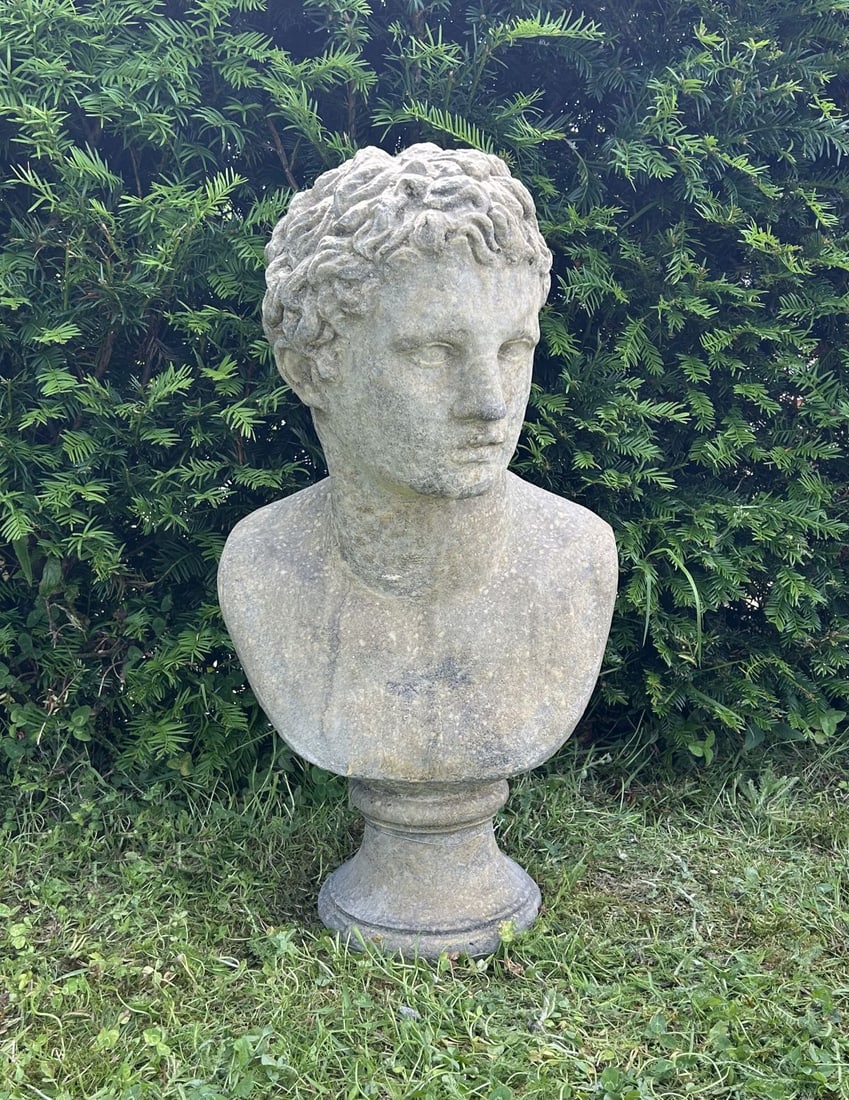 COMPOSITE STONE BUST OF ADONIS: Composite stone bust of Adonis with youthful classical features, raised on a circular socle. Weathered surface patination.