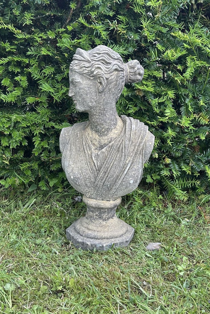 COMPOSITE STONE BUST OF APHRODITE: Composite stone bust of Aphrodite draped in classical robes and raised on a circular socle and square plinth base. Weathered surface patination.