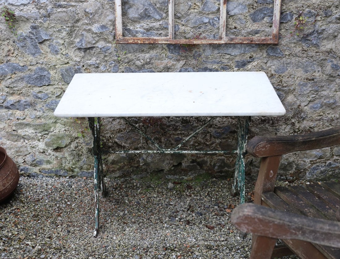 19TH-CENTURY CAST IRON GARDEN TABLE: The rectangular marble top raised on cast iron scroll end supports with decorative foliate and scroll ornament throughout. Retaining traces of original green painted finish.