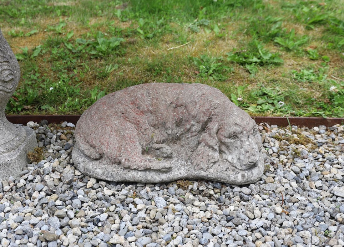 COMPOSITE STONE RECUMBENT CANINE: Modelled asleep with curled tail and flowing coat retaining traces of original surface colouring.