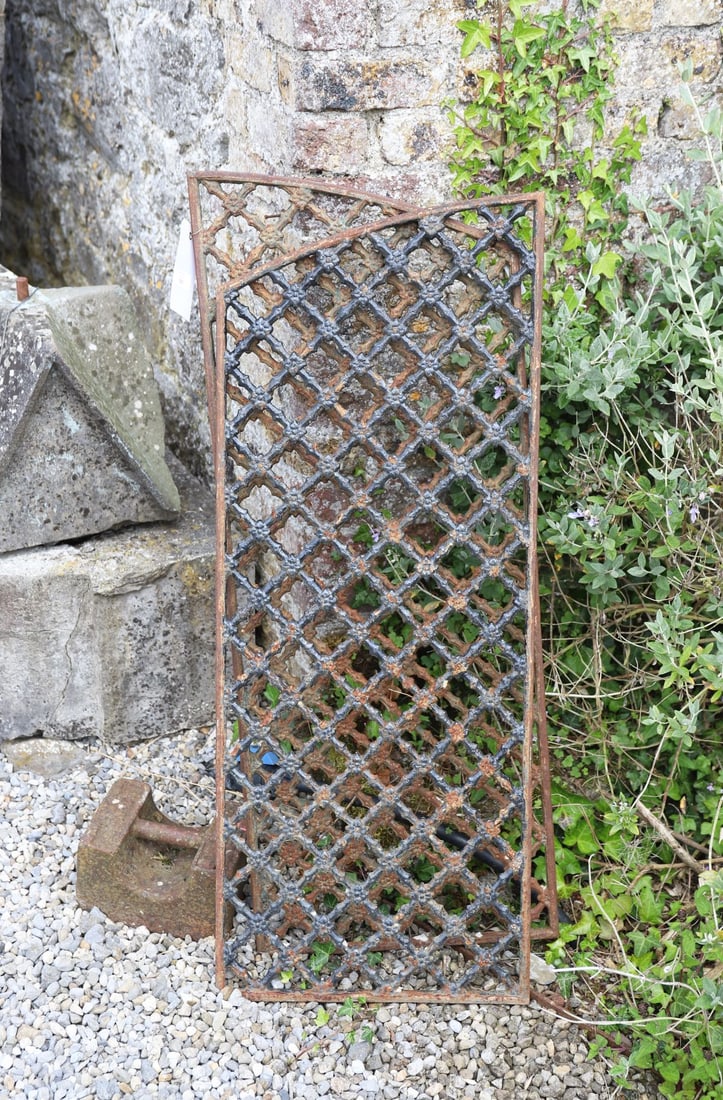 PAIR OF CAST IRON ARCHED LATTICE PANELS: A pair of heavy cast iron latticework panels, each with a rounded top and repeating diamond pattern, set with central quatrefoil-like detailing. Substantial and well-weathered, with surface rust and r
