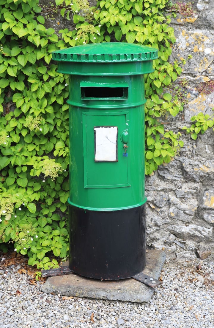 GREEN PAINTED METAL PILLAR POST BOX: A traditional-style pillar post box in cast metal, painted green. Domed top and vertical letter slot, suitable for garden or decorative display.