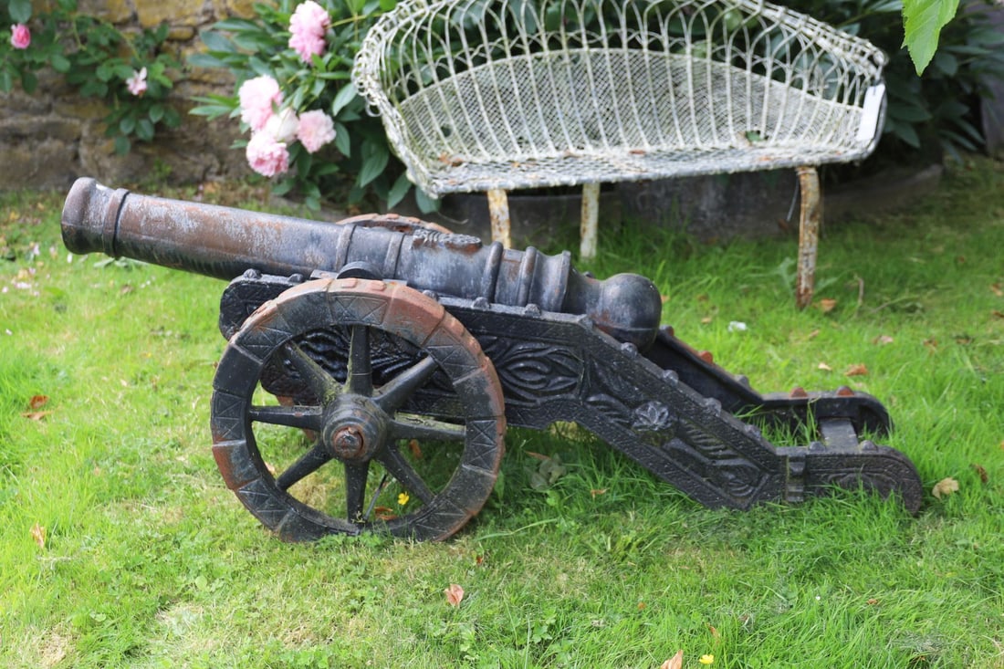 CAST IRON CANNON ON CARRIAGE: Cast iron cannon mounted upon a wheeled carriage with decorative side panels.