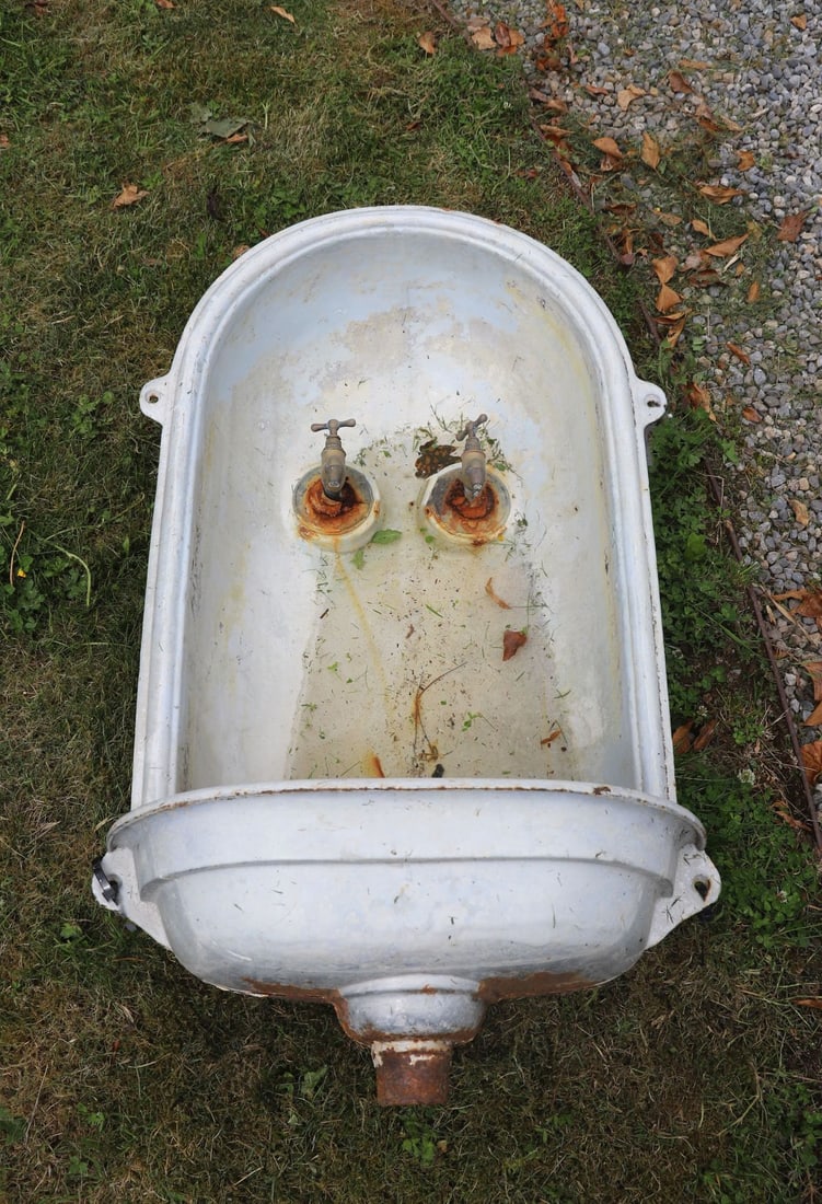 EARLY 20TH-CENTURY GALVANISED CAST IRON BASIN: WALL-MOUNTED The deep oval basin with rolled rim, fitted with a pair of brass taps and rear wall-mounting lugs, terminating in a central waste outlet. Weathered industrial surface with age-related pat
