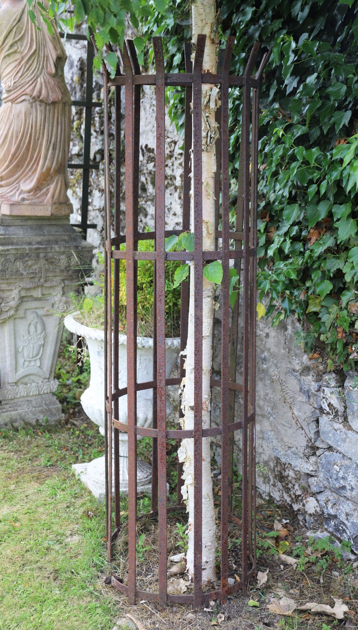 VICTORIAN WROUGHT IRON TREE GUARD: Victorian wrought iron tree guard of cylindrical form with vertical bars and riveted construction.