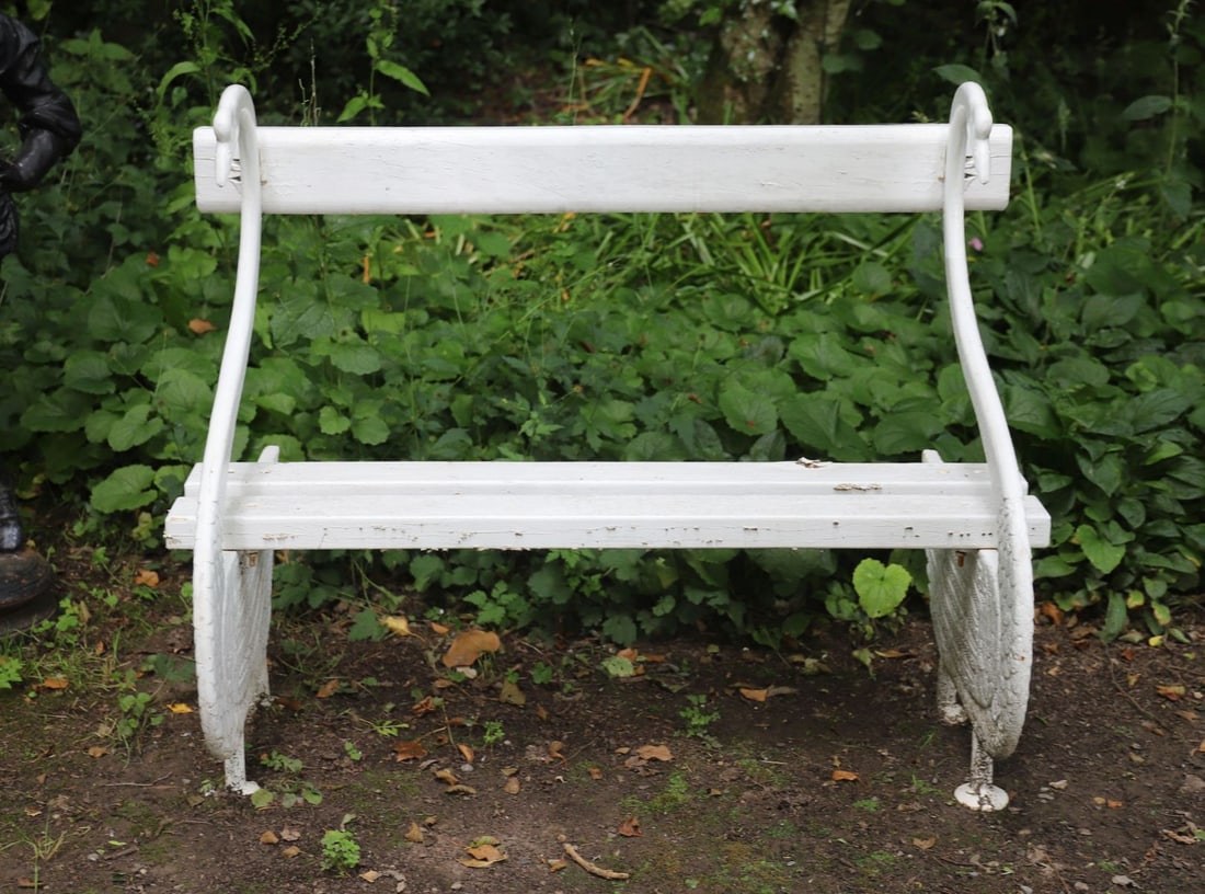 WHITE PAINTED CAST IRON SWAN BENCH: A whimsical cast iron garden bench modelled with swan-form end supports and shaped wooden slats forming the seat and backrest. Painted white with minor surface wear.