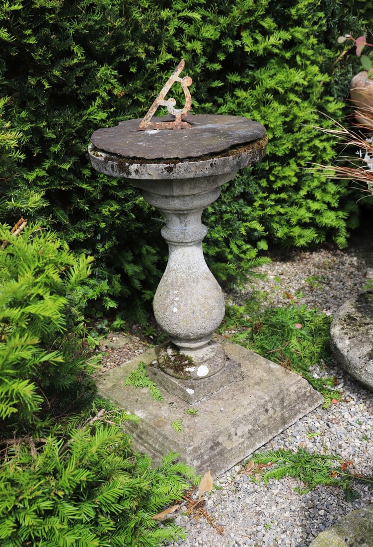 STONE PEDESTAL SUNDIAL TABLE: Stone pedestal table with circular top, surmounted by an iron sundial gnomon, raised on a baluster-form pedestal and square stepped base. Weathered surface throughout.