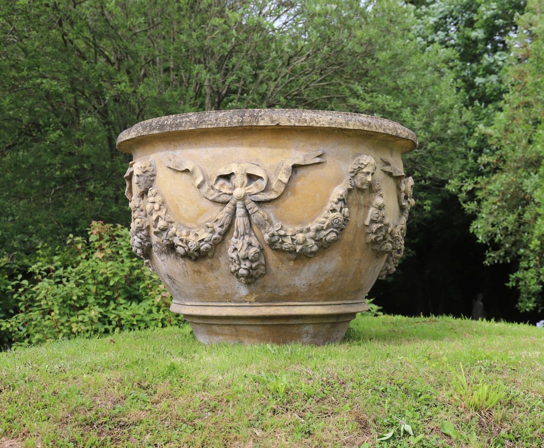 MONUMENTAL COMPOSITE STONE GARDEN PLANTER: Large circular garden planter with moulded rim and richly cast garland and ribbon decoration interspersed with classical masks, raised on a substantial square pedestal base.