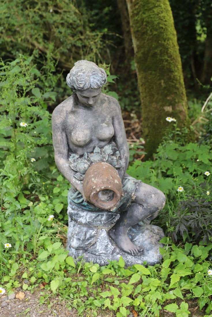 COMPOSITE STONE FIGURAL GARDEN FOUNTAIN: Modelled as a seated maiden holding an overturned urn amongst fruit, with aged verdigris-effect patination.