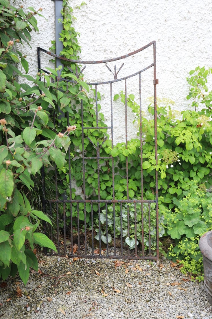 19TH-CENTURY WROUGHT IRON GARDEN GATE: The inverted arched top above vertical bars and stylised foliate motifs, retaining traces of original paint beneath weathered surface patination.