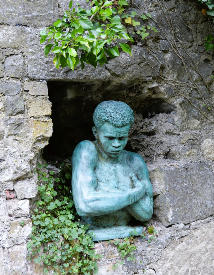 BRONZE SCULPTURE OF A MALE WITH FOLDED ARMS: A modern bronze sculpture depicting a standing male figure with arms folded. Stylised form with textured surface and contemplative posture.