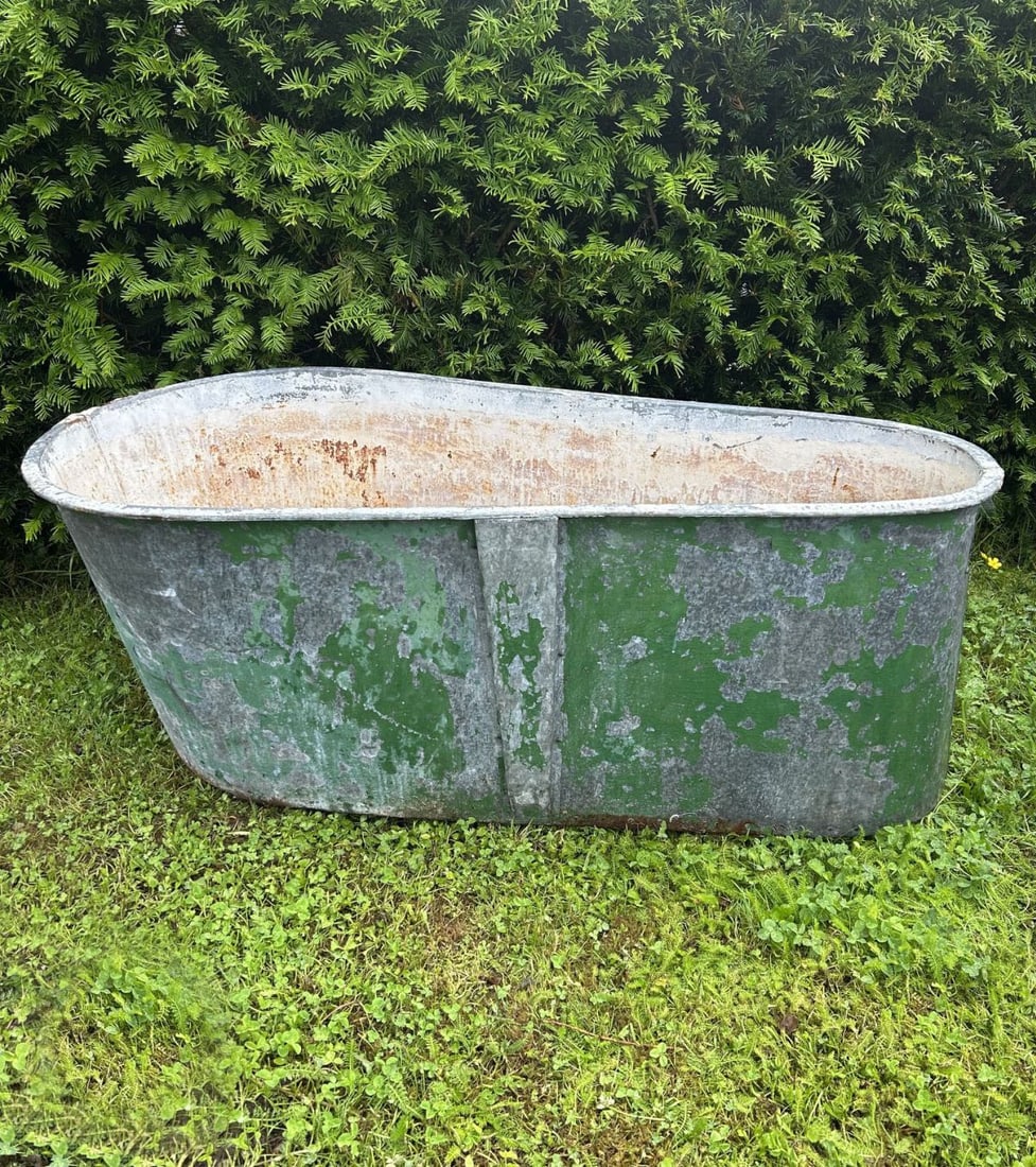 VINTAGE ZINC BATH: Large galvanised bath of oval form raised on shaped supports, retaining traces of original green paint.