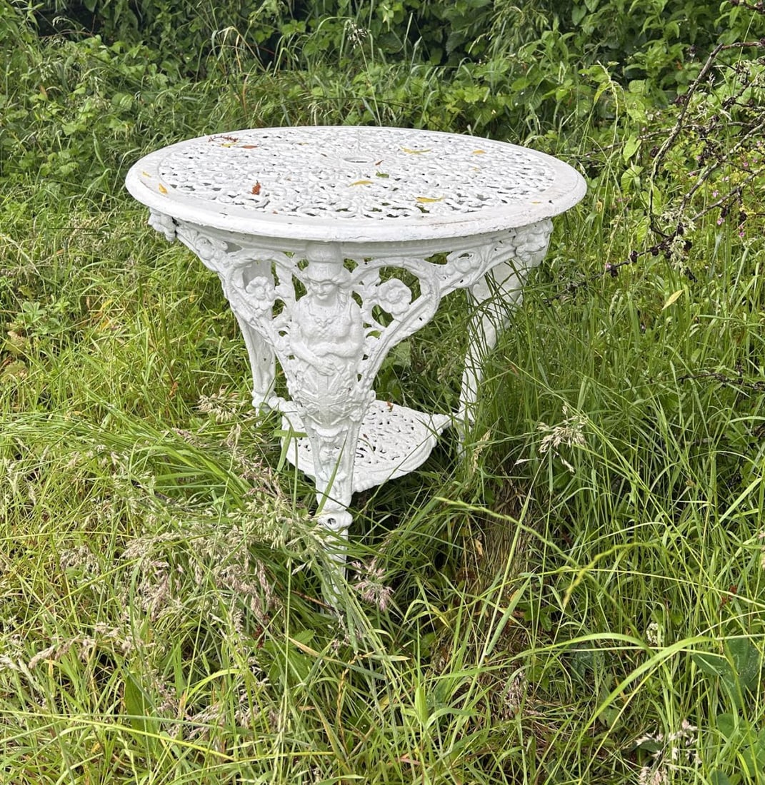 VICTORIAN CAST IRON GARDEN TABLE: Victorian cast iron garden table with circular pierced top decorated with scrolling foliage and floral motifs, raised on ornate figural supports united by an undertier. Painted finish.