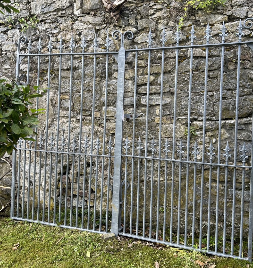 ESTATE CAST AND WROUGHT IRON ENTRANCE GATES: A substantial pair of entrance gates incorporating cast iron fleur-de-lis finials and scrollwork cresting above wrought iron rails and stiles, of traditional estate form. Galvanised finish throughout.