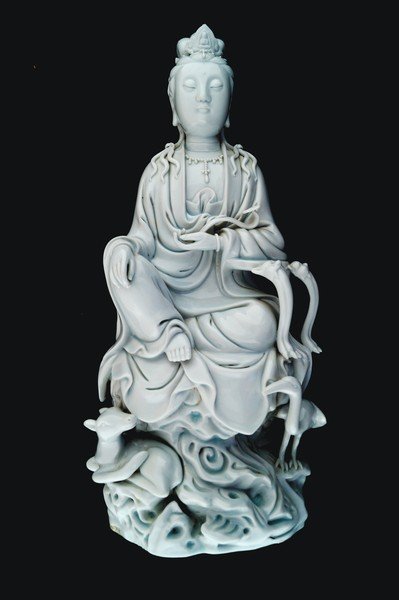 A Chinese blanc de Chine figure of Guanyin: flanked by a deer and a crane. The goddess crowned with a tiara set with the Amitabha Buddha, resting her left arm against a table and cradling a ruyi sceptre, her right hand resting on her right knee