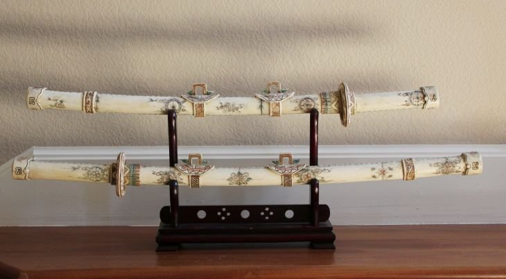 BONE SWORD SET 32" - HAND CARVED: BONE SWORD SET - VERY DETAILED HAND CARVING - L: 32", D: 4", H: 14" - ROSEWOOD STAND - UPPER SWORD IS 32" LONG - THE LOWER SWORD IS 28"LONG - MINT CONDITION