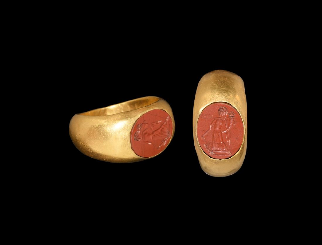 Roman Gold Ring with Fortuna Intaglio: 1st-2nd century AD. A gold ring with D-section hoop widening at the shoulders; flat bezel set with a jasper intaglio engraved with standing figure of Fortuna holding cornucopia and rudder. 6.88 grams,