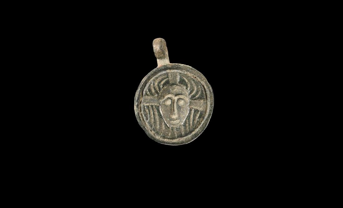Byzantine Pendant with Corpus Christi: 7th-10th century AD. A bronze discoid plaque with integral suspension loop above, mask of Christ facing on a textured field with radiating arms of the cross behind. 2.69 grams, 21mm (3/4"). Property o