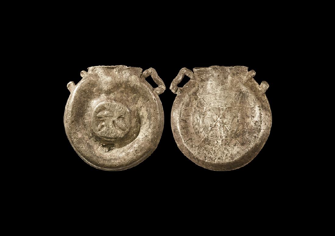 Medieval Pilgrim's Ampulla: 13th century AD. A hollow high tin small ampulla with flat circular body, one loop at short neck; to one side geometric decoration formed from thin lines, a raised man and tree (?) decoration to the r