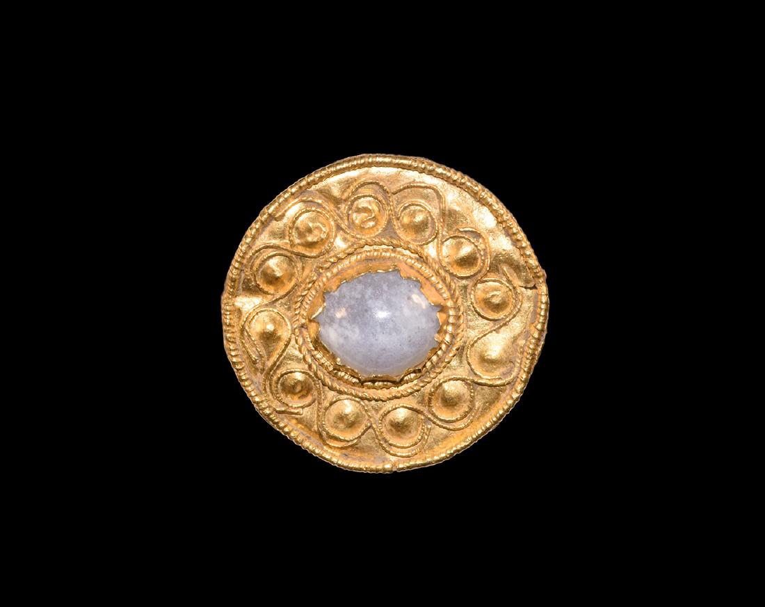 Eastern Greek Gold Jewelled Plate Brooch: 5th-3rd century BC. A discoid sheet gold plate brooch with beaded wire border, running scroll filigree band, central cell within two concentric filigree collars, inset later agate cabochon; loop and c