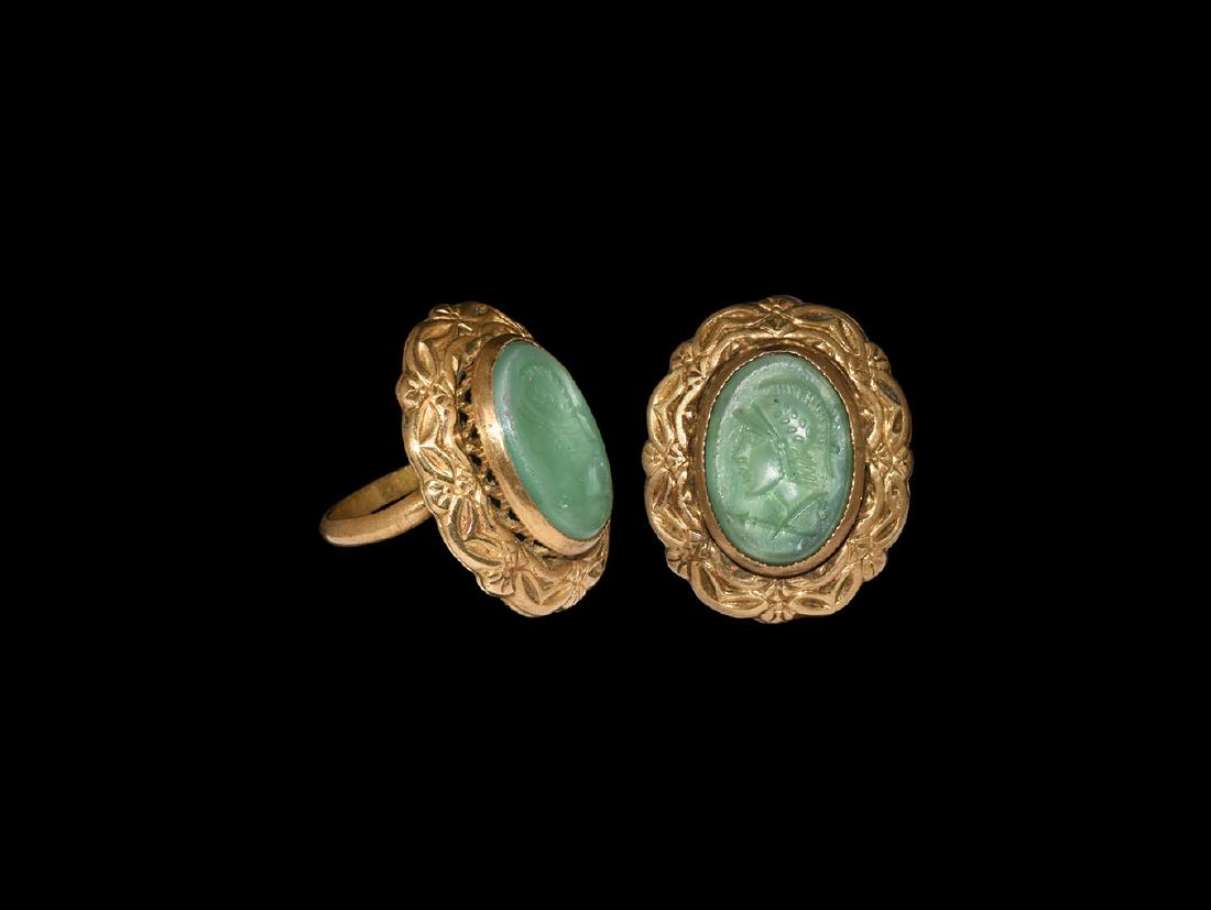Gilt Grand Tour Ring with Helmetted Bust Intaglio: 19th century AD. A gilt metal finger ring comprising a D-section hoop, applied plaque with band of swags and rosettes, openwork cell with inset green glass cloison, intaglio helmetted bust of Mars and