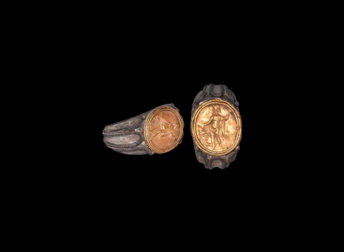 Roman Silver Ring with Gold Intaglio: 2nd-3rd century AD. A cast ring with tapered band with three moulded channels, flaring out at shoulders; the bezel with much later inset gold repoussÃ© oval depicting a standing semi-nude male figur
