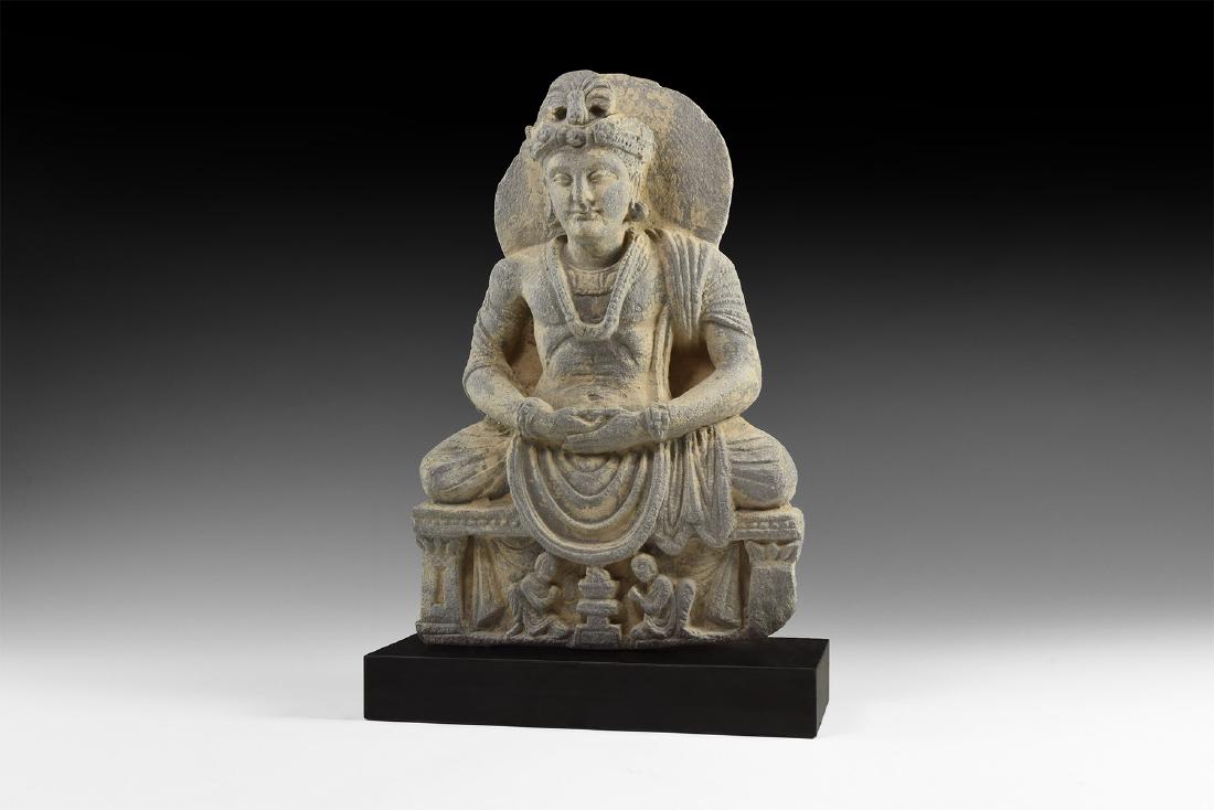 Gandharan Buddha Statuette: 2nd-4th century AD. A carved schist statuette of Buddha sitting facing in loose garment, hands folded in the lap, nimbus behind the head, dais with flaming altar and two worshippers; mounted on a cust