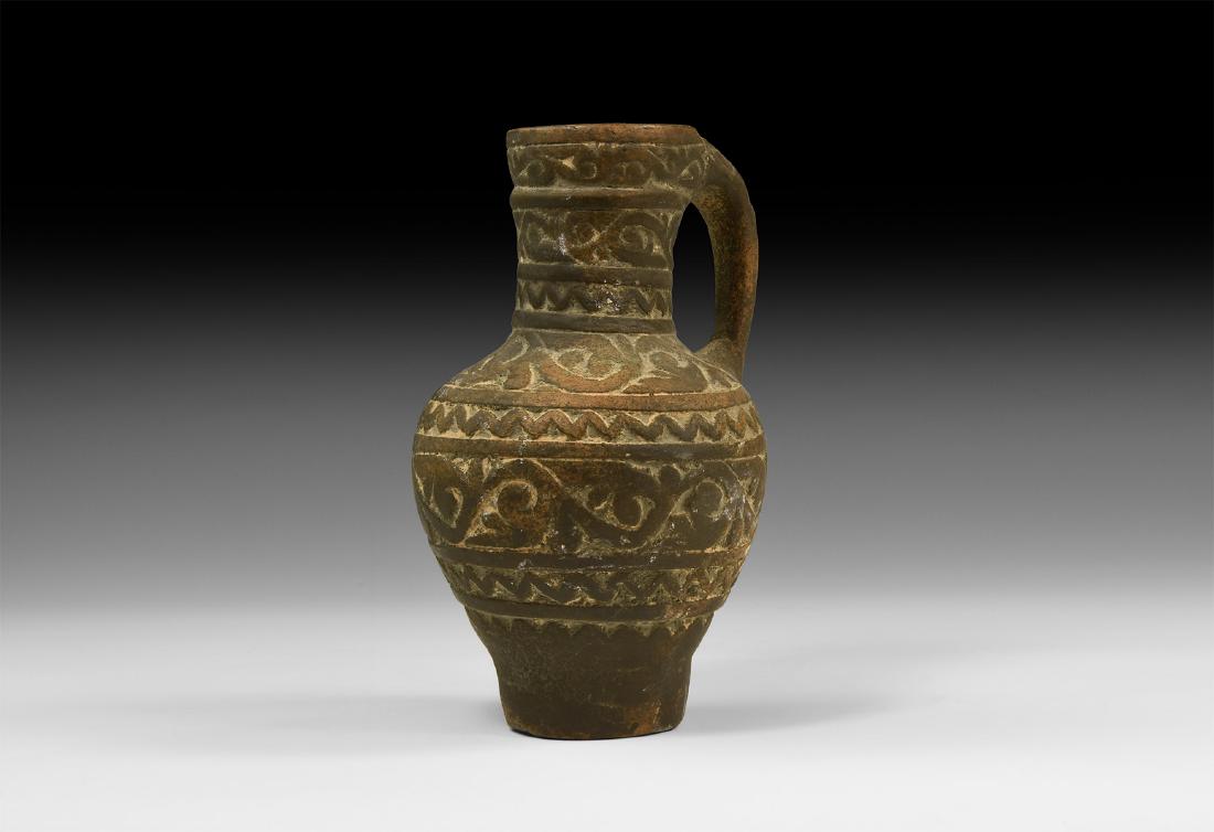 Islamic Ceramic Jug: An undated archaistic earthenware jug with piriform body and strap handle, bands of reserved scrolled tendril and zigzag decoration. 375 grams, 16cm (7 1/4"). Property of a London gentleman; acquired 