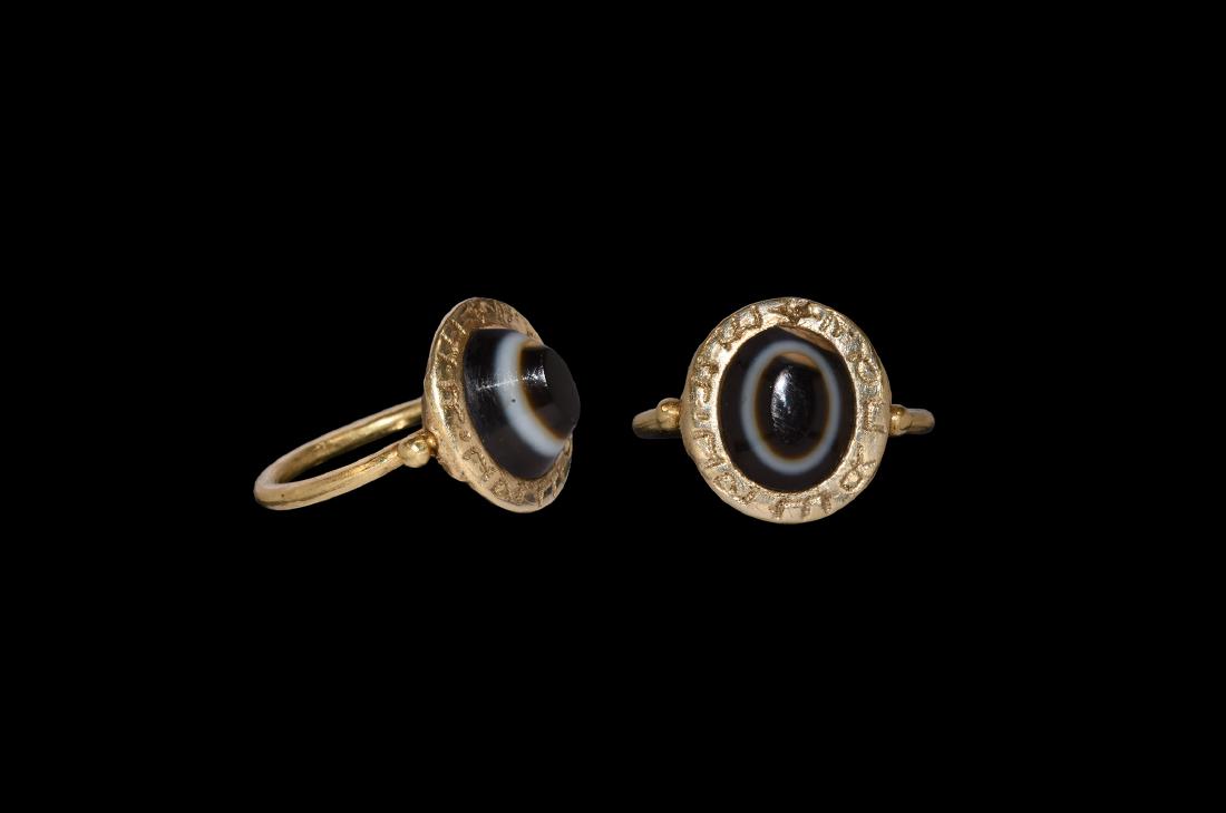 Medieval Gold Ring with Inscription: 15th-16th century AD. A gold ring comprising a round-section hoop with large granule to each shoulder, pie-dish bezel with earlier inset banded agate cabochon, enigmatic inscription to the rim ''*M?'?