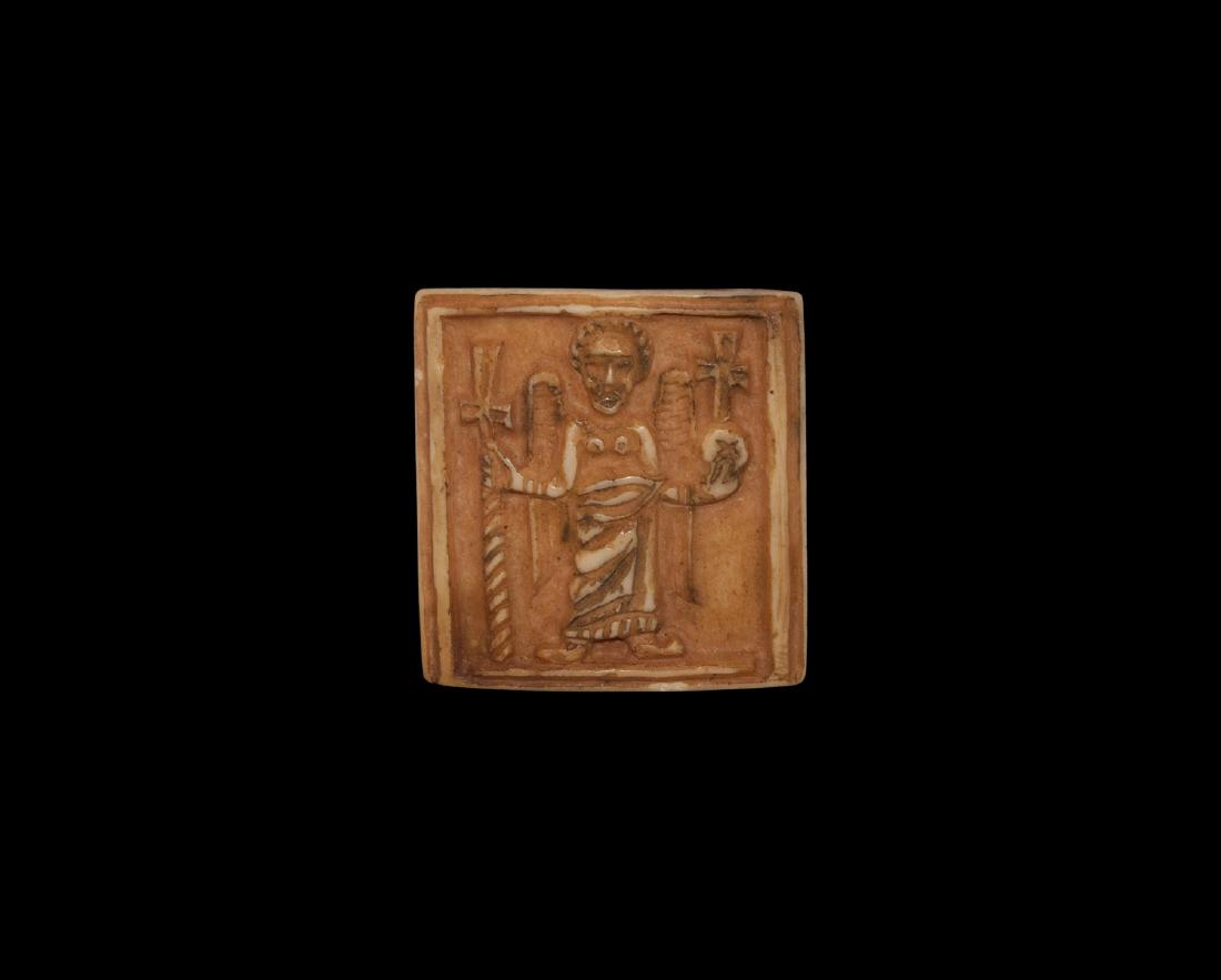 Post Medieval Bone Plaque with Saint: 19th century AD. A square carved bone plaque, curved in profile with raised border, facing robed figure with beaded nimbus and folded wings, holding an orb in the left hand surmounted by a voided cros