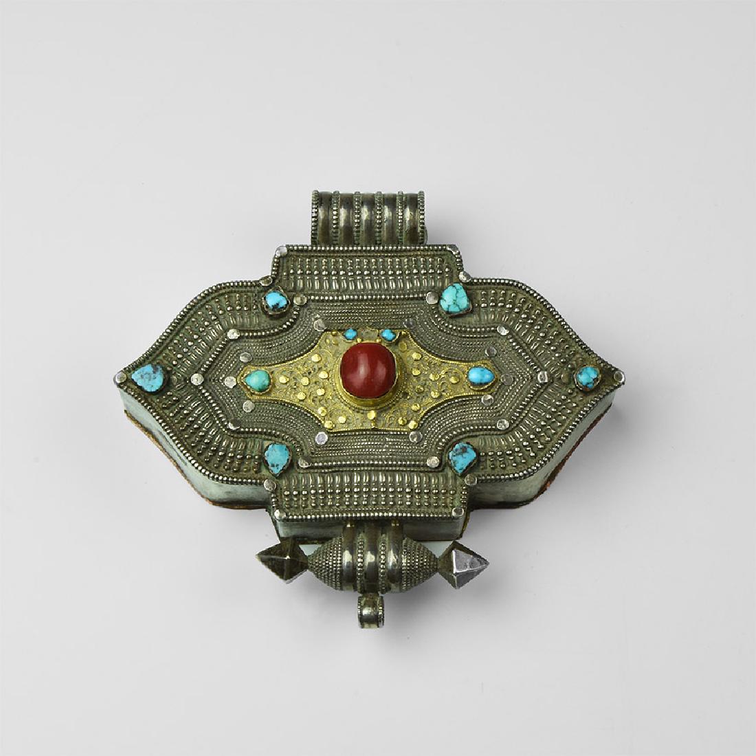 Tibetan Jewelled Amulet Box: 20th century AD. A silver-coloured metal Tibetan Gau amulet box in double ogival form with cloison coral to the centre and cloison turquoise stones to the corners; infilled with repoussé border of pe