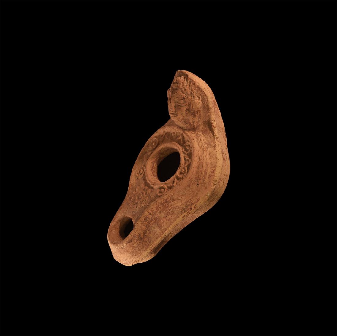 Byzantine Oil Lamp with Face: 6th-9th century AD. A slipper-shaped oil lamp with pellet-and-annulet and chevron decoration, wreath to the outer rim, the handle formed as a female head with curled hair, wearing a headdress with vei