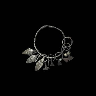 Viking Silver Bracelet with Amulets: 10th-12th century AD. A silver bracelet with ends twisted round the twisted wire loop, amuletic pendants including twisted wire rings, miniature axe-blades, miniature lozenge faces, miniature firestri