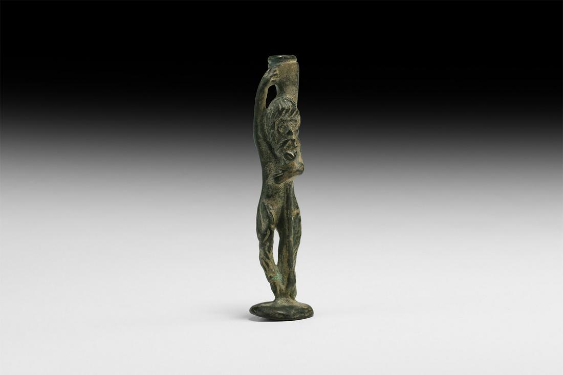 Roman Faunus Statuette: 1st-2nd century AD. A bronze statuette of Faunus (Greek Pan) standing on a circular base, long hair and beard, leaning on a short stick(?), carrying a wine jug on his left shoulder supported by his ri